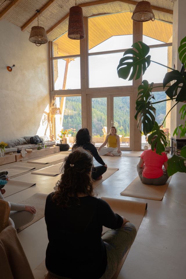 Gruppe sitzt in Meditation, warmes Licht fällt durch die großen Fenster