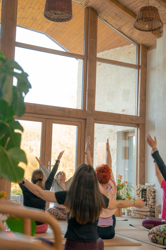 Yogagruppe mit weit geöffneten Armen vor großen Fenstern
